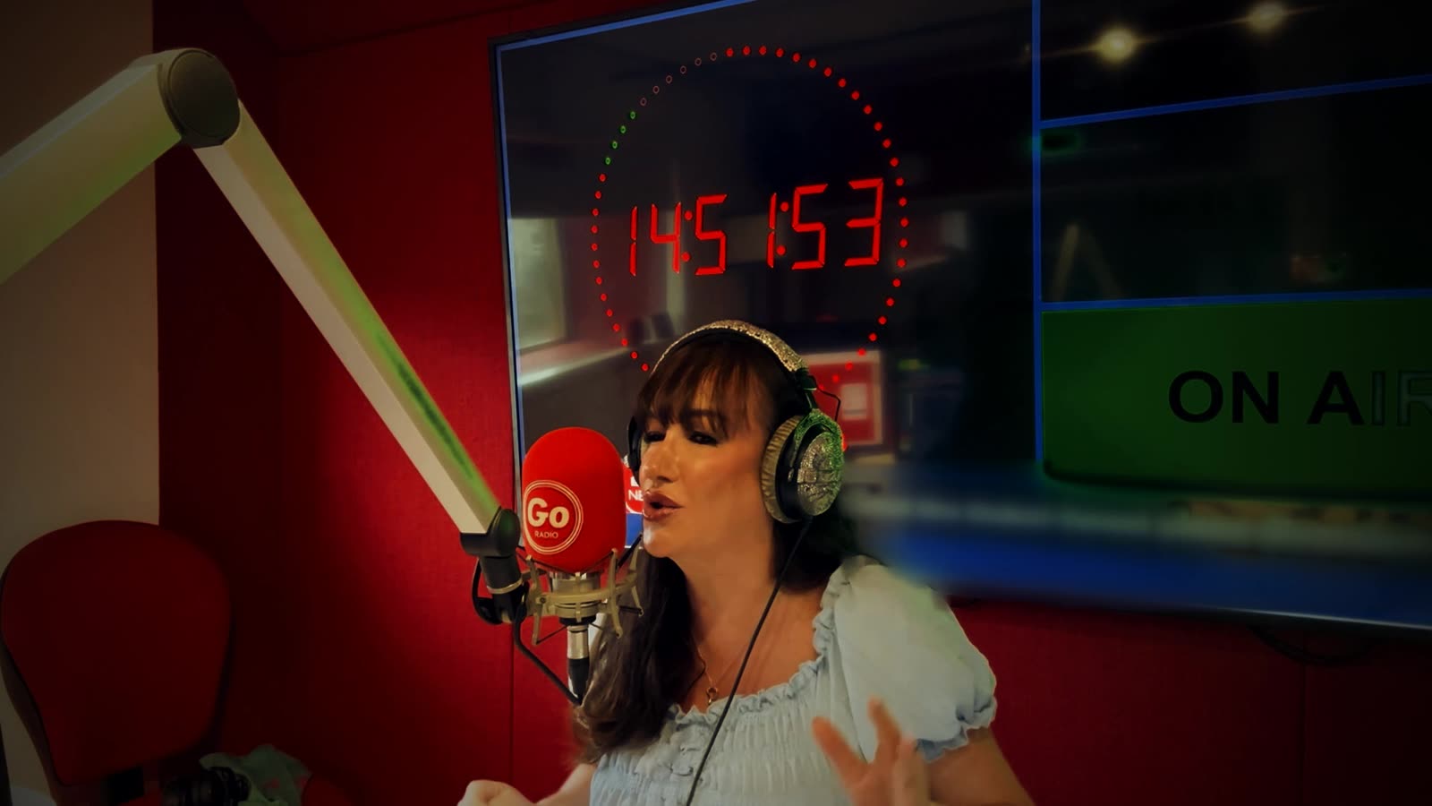 Gina McKie on air in the Go Radio studio, headphones on, speaking into the red Go microphone